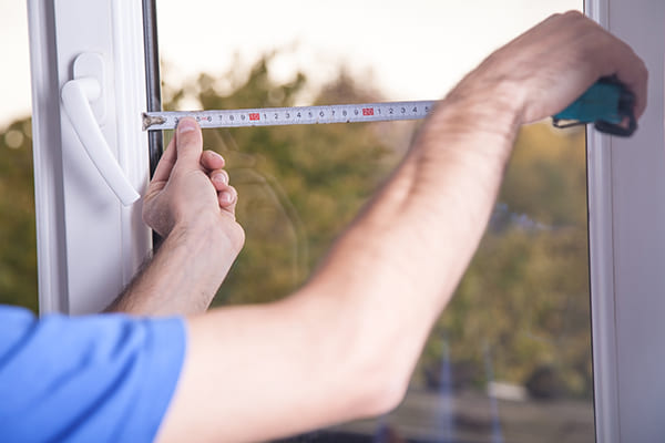 Ouvrier mesurant la largeur d'une fenêtre avec un mètre ruban